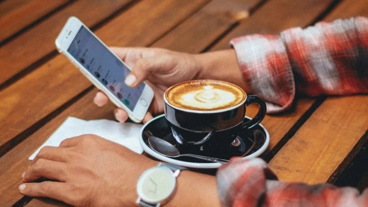 A person using a phone beside a warm drink