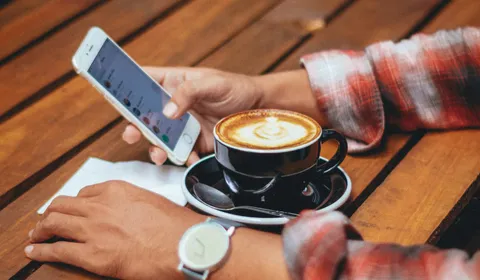 A person using a phone beside a warm drink